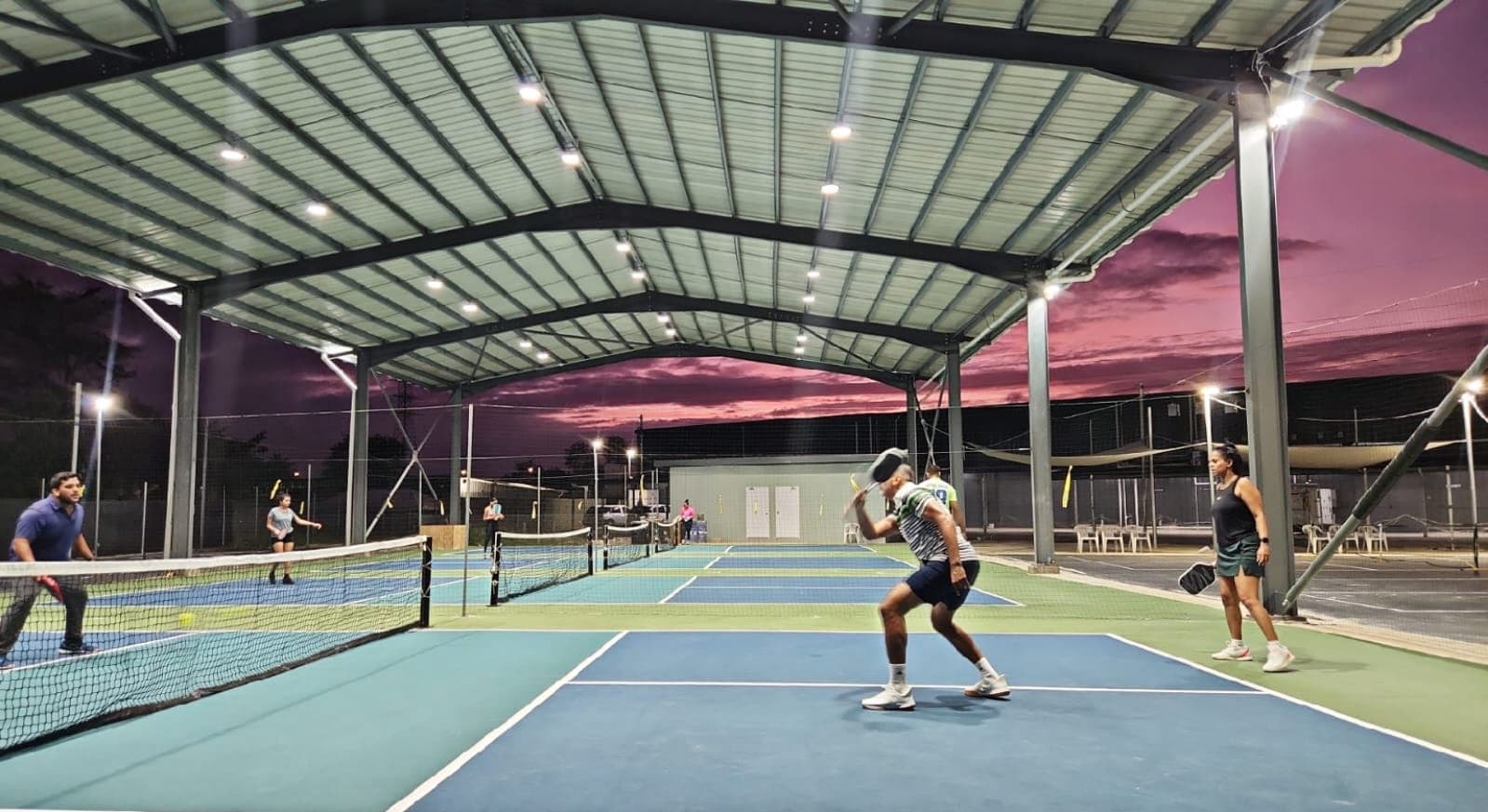 Doubles pickleball rally under the covered roof at sunset