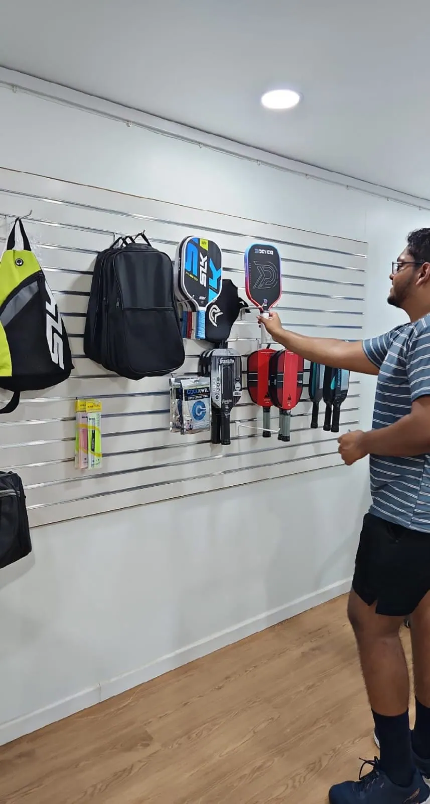 A player choosing a paddle from the pro-shop wall display of paddles, bags and accessories at the venue